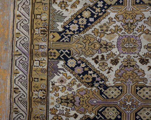 Intricate gold, navy, and lavender patterned rug border next to distressed wood flooring.