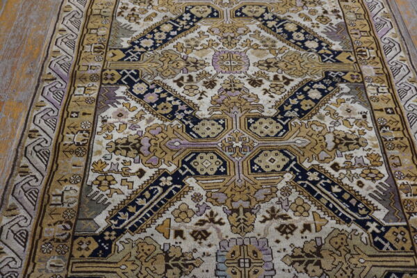 A cream rug with elaborate gold, navy, and purple geometric patterns rests on wooden flooring.