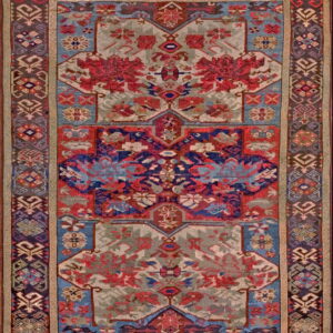 Rectangular rug featuring intricate geometric motifs in crimson, navy, light blue, and muted gray with dark patterned borders.
