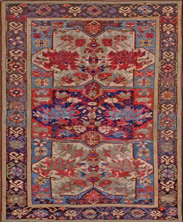 Rectangular rug featuring intricate geometric motifs in crimson, navy, light blue, and muted gray with dark patterned borders.