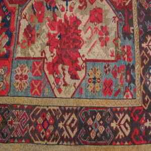 Tight weave rug detail showing red and tan stylized florals, dark borders, and wood floor context.