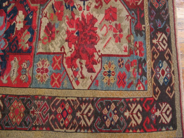 Tight weave rug detail showing red and tan stylized florals, dark borders, and wood floor context.