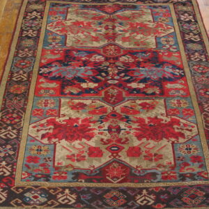 Muted red, taupe, and blue geometric patterned rug displayed on warm wooden plank flooring.