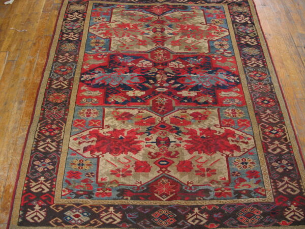 Muted red, taupe, and blue geometric patterned rug displayed on warm wooden plank flooring.