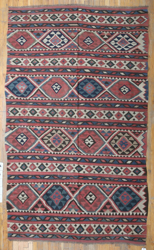 Flatwoven rug with red, navy blue, and cream geometric diamond patterns over light wood planks.
