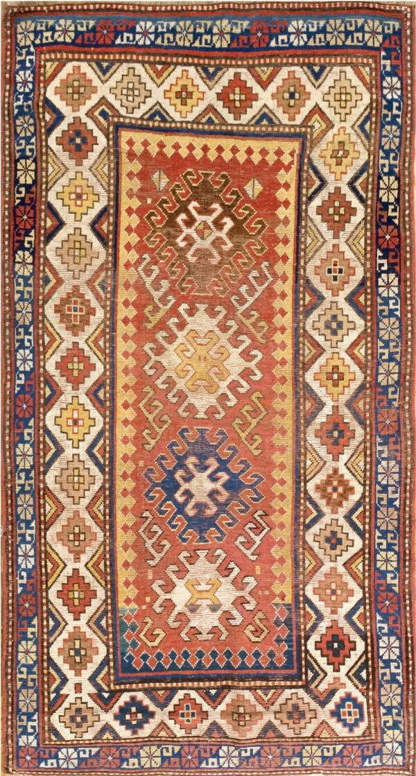 A low-pile geometric rug featuring a rust red central field and multi-layered cream, blue, and yellow borders.