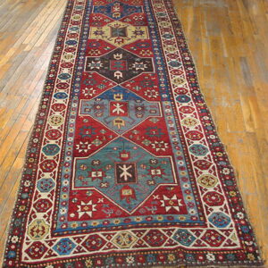 Low-pile geometric runner rug in red, teal, and cream colors laid on distressed wood flooring.