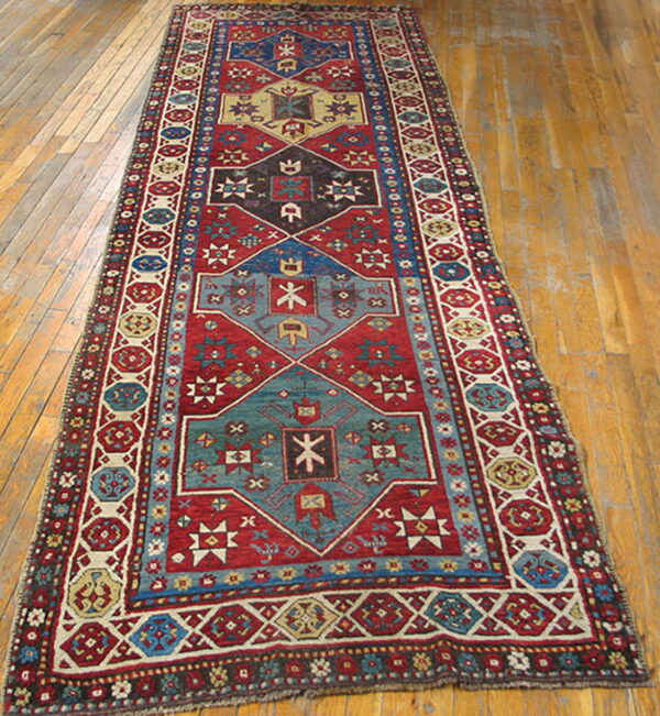 Low-pile geometric runner rug in red, teal, and cream colors laid on distressed wood flooring.