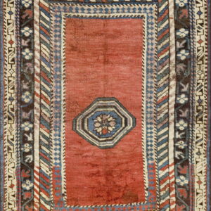Rectangular rug with a faded red field, centered octagon, and detailed geometric borders in blue, cream, and brown.