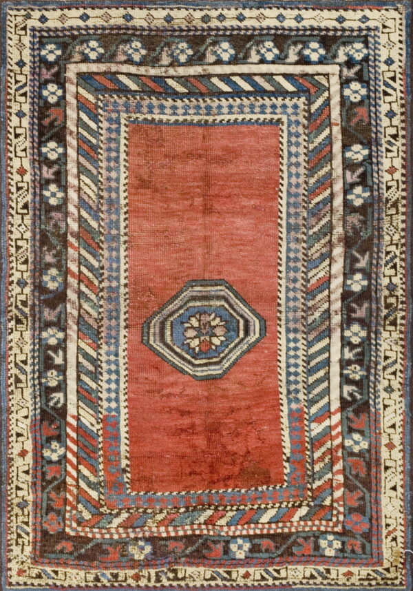 Rectangular rug with a faded red field, centered octagon, and detailed geometric borders in blue, cream, and brown.