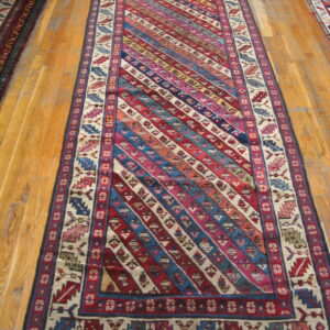 A long, multi-colored runner rug featuring diagonal geometric stripes and patterned borders on hardwood.