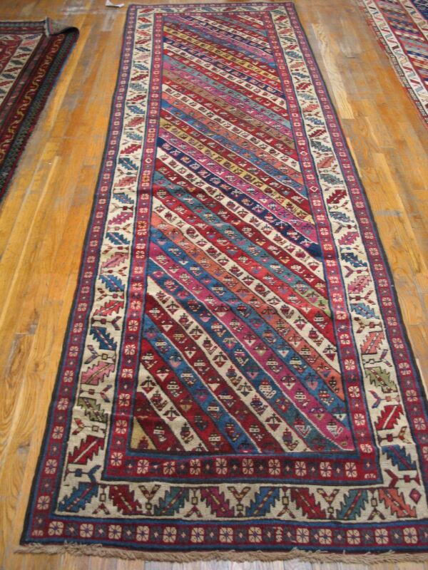 A long, multi-colored runner rug featuring diagonal geometric stripes and patterned borders on hardwood.