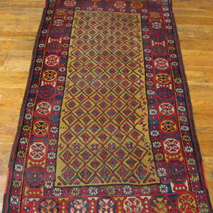 Red and gold diamond pattern rug with wide geometric borders on a warm wooden floor.