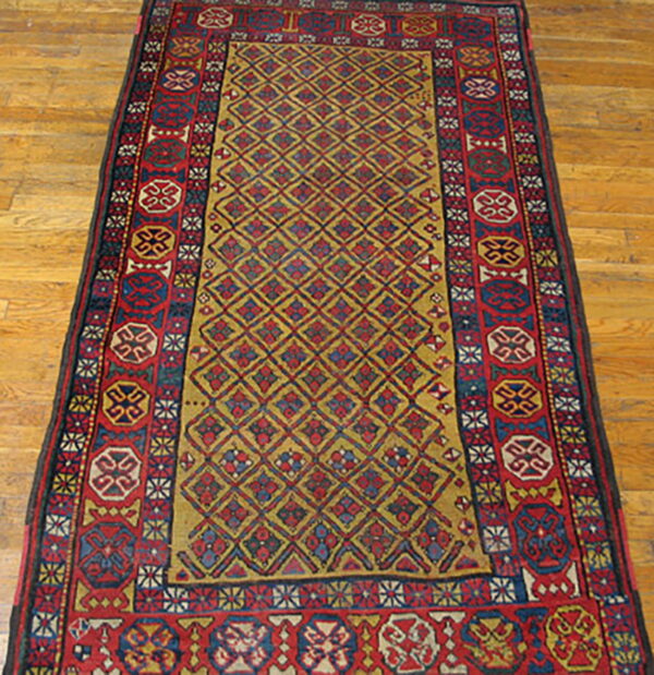 Red and gold diamond pattern rug with wide geometric borders on a warm wooden floor.