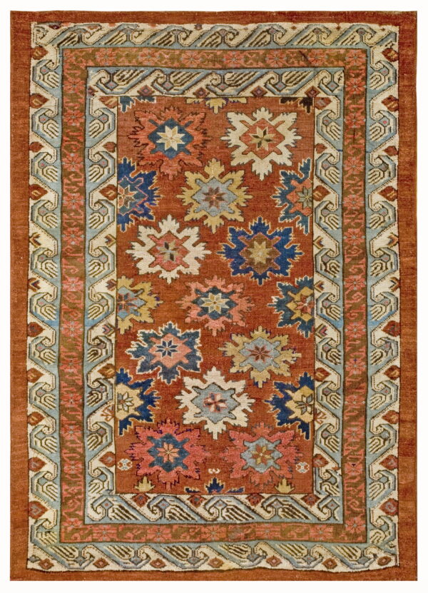 Rust colored rug with repeating blue, pink, and cream star motifs bordered by intricate geometric patterns.