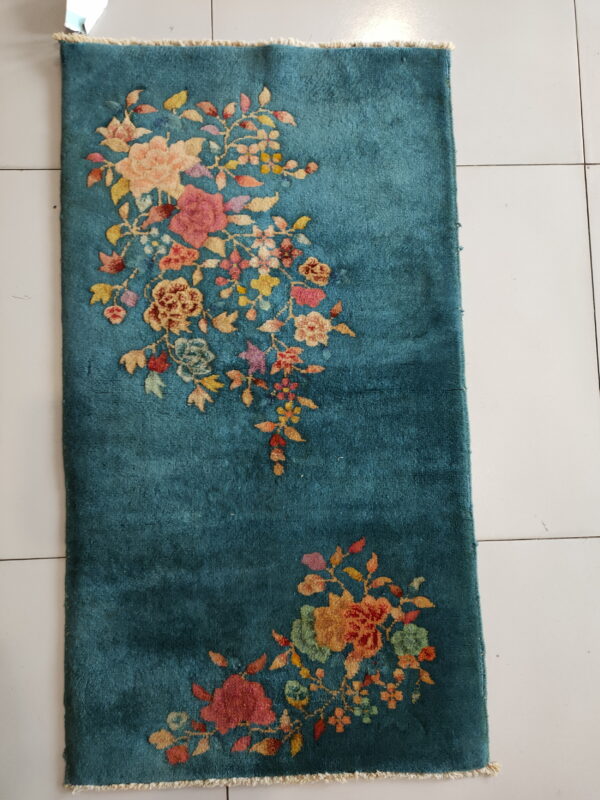 Teal runner rug featuring an asymmetrical floral pattern in pink, yellow, and red on white tile flooring.