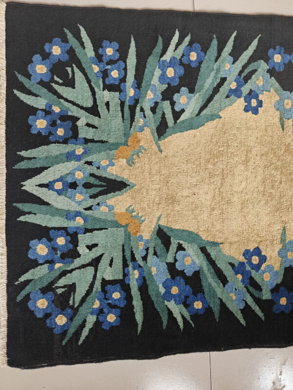 Dark floral rug featuring a dense blue and green border surrounding a large, plain tan central field.