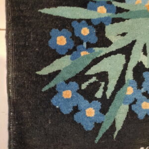Dark floral rug detail showing blue and yellow flowers, green foliage, and white fringe on light tile.