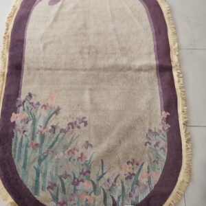 Light beige oval rug featuring a dark purple border and a multicolored botanical pattern at the bottom.