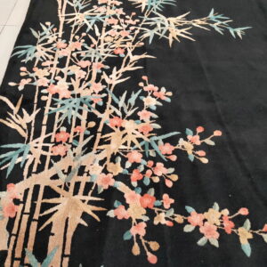 Plush black rug displaying a large botanical pattern of pink blossoms and tan bamboo on a tiled floor.