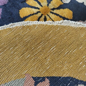 Close-up showing a high-pile floral rug face next to its tightly woven mustard-colored backing.