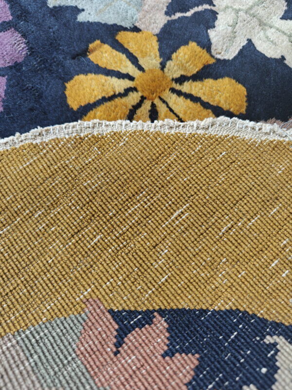 Close-up showing a high-pile floral rug face next to its tightly woven mustard-colored backing.
