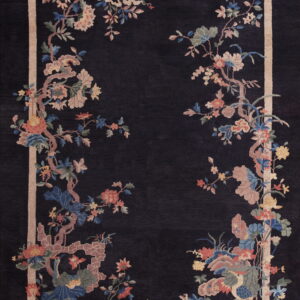 Deep indigo rug with a sprawling botanical pattern of pink, blue, and yellow flowers, enclosed by a tan frame.