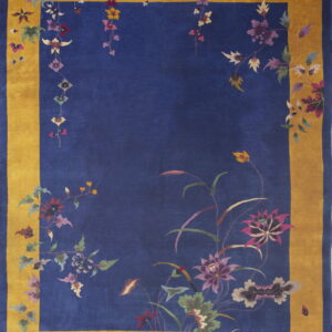 A deep blue rug features a wide gold border and stylized floral vines in purple, pink, and green.