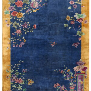 A royal blue rug with a wide gold border features multi-colored botanical motifs concentrated in the corners.