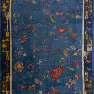 Deep blue rug with large rust and pink floral motifs, framed by a dark blue and gold key border.