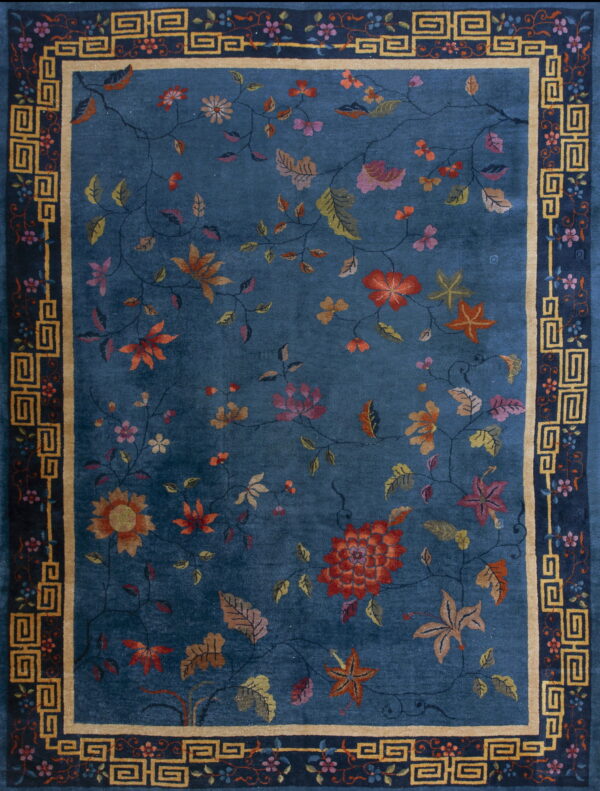 Deep blue rug with large rust and pink floral motifs, framed by a dark blue and gold key border.