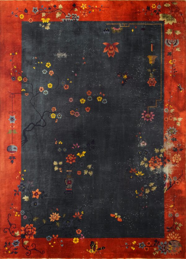 Corner of a deep red low-pile rug with natural fringe rests on rustic wood flooring near an inventory tag.