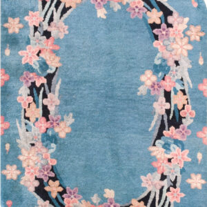 Plush aqua rug featuring a colorful floral border, rounded ends, and cream fringe on a light tiled floor.