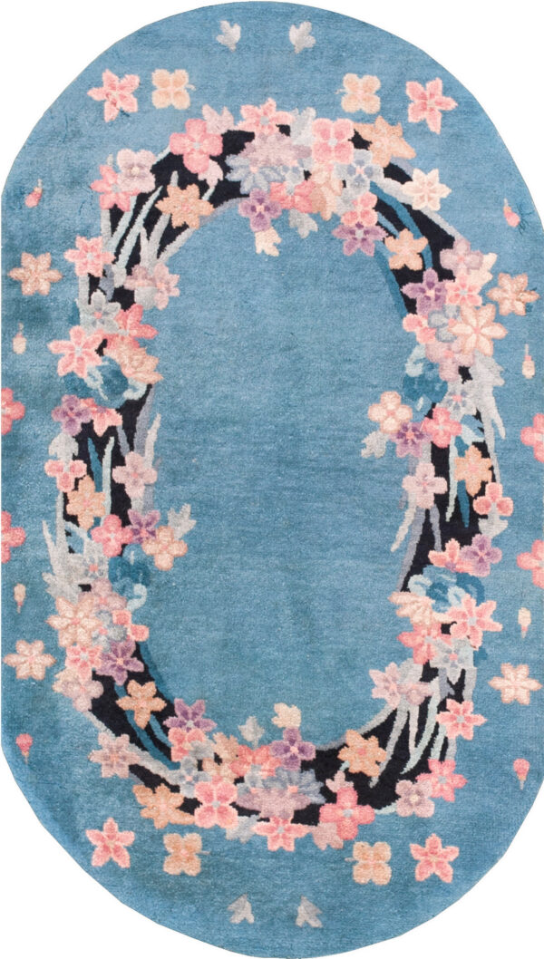 Plush aqua rug featuring a colorful floral border, rounded ends, and cream fringe on a light tiled floor.