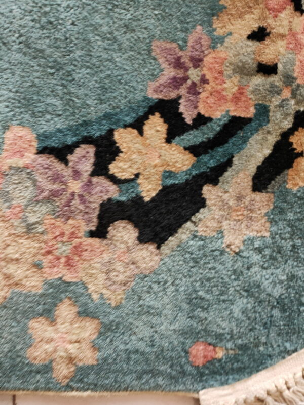 A teal, high-pile rug detail featuring large stylized flowers in beige, salmon, purple, and black.