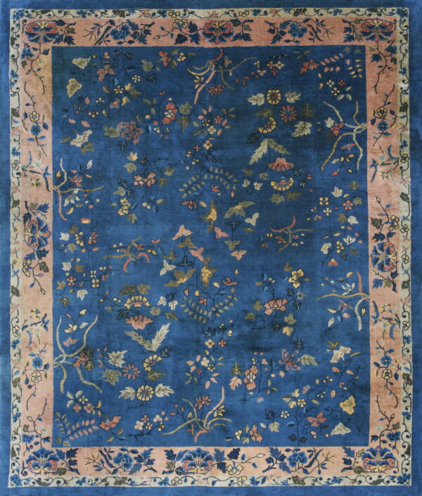 Deep blue rug with scattered flowers and butterflies, framed by a wide peach pink border.