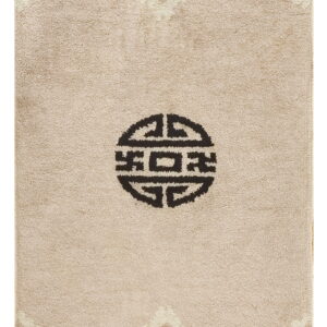 A beige high-pile rug features a central dark symbol and multicolored abstract borders at the top and bottom.