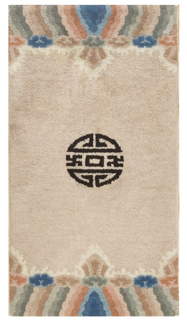 A beige high-pile rug features a central dark symbol and multicolored abstract borders at the top and bottom.