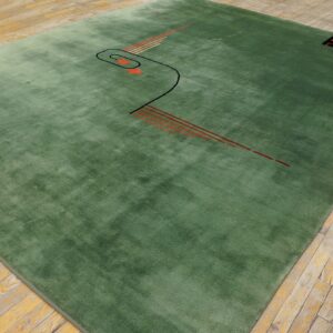 Plush sage green rug displaying abstract black and orange geometric patterns is laid on distressed wood planks.