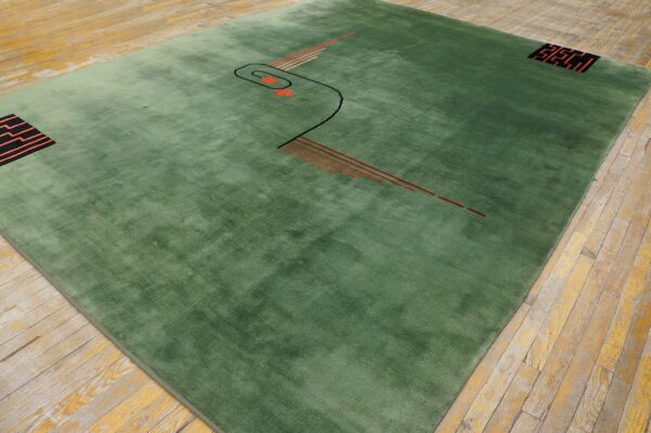 Plush sage green rug displaying abstract black and orange geometric patterns is laid on distressed wood planks.