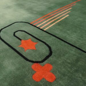 Green rug with a high pile and abstract black lines framing red-orange shapes and warm diagonal stripes.