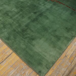 A smooth green rug, accented by red dashes, lies on distressed yellow wooden plank flooring.