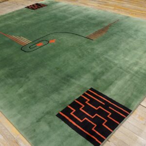Low-pile green rug with abstract black and orange geometric patterns lies on worn wooden flooring.