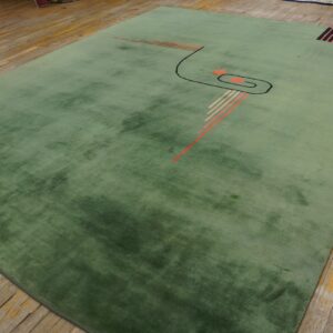 Muted green high-pile rug with abstract geometric accents rests on distressed hardwood flooring.