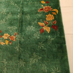 Deep green plush rug with carved foliage patterns and colorful orange, red, and gold floral accents.