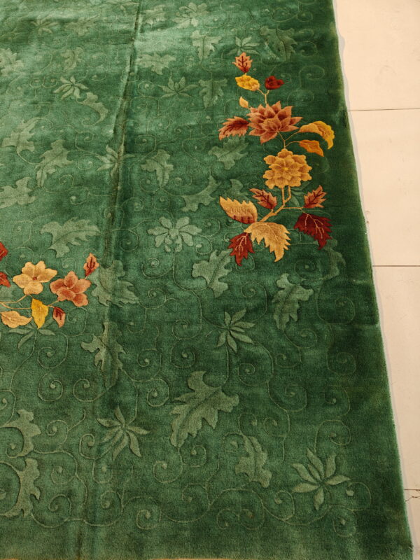 Deep green plush rug with carved foliage patterns and colorful orange, red, and gold floral accents.