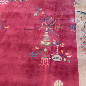 Plush deep pink rug featuring intricate multicolored botanical and vase motifs near a beige border.