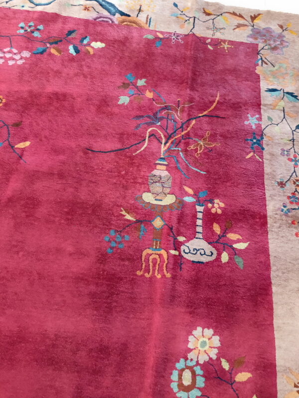 Plush deep pink rug featuring intricate multicolored botanical and vase motifs near a beige border.