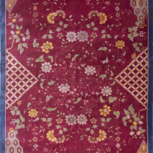 A maroon rug with sprawling yellow, gray, and green florals, framed by a navy blue border and geometric corners.