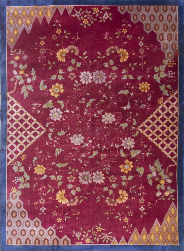 A maroon rug with sprawling yellow, gray, and green florals, framed by a navy blue border and geometric corners.